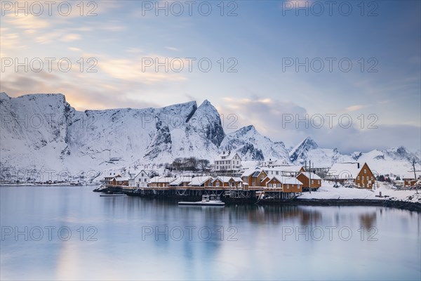 Traditional yellow rorbuer huts on the island of Sakrisoy, snow-capped mountains in the background,