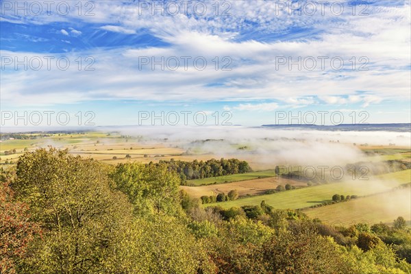 View of a patchwork landscape in the countryside with fog above the fields and beautiful autumn