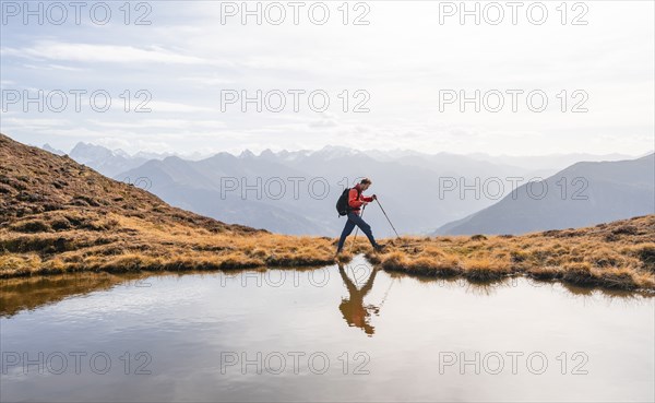 Mountaineer hiking with poles, reflected in a small mountain lake on the Krahberg, mountain