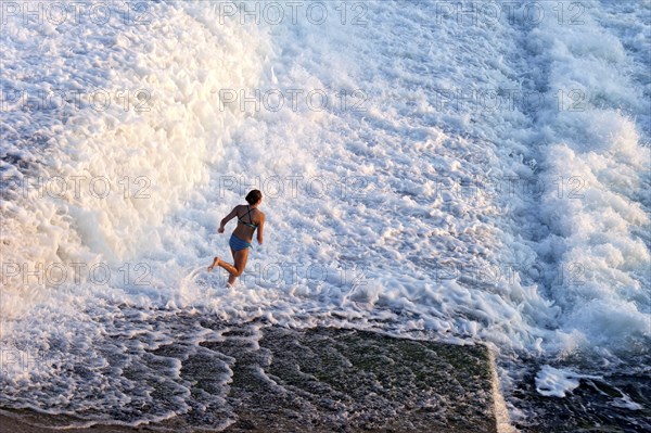 Girl bathing in the spray of the Lech weir, jumping into the white foaming water of the cascades,