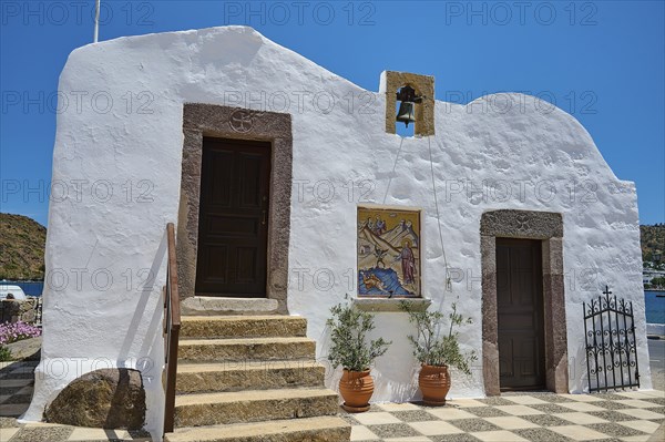 White building in traditional Greek style with staircase, two doors and bell, under blue sky and in