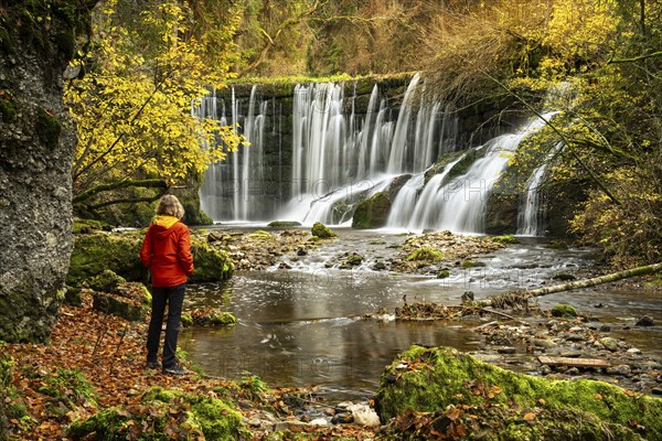 The Geratser waterfall in autumn. A hiker stands on the bank. Moss-covered rocks and trees in