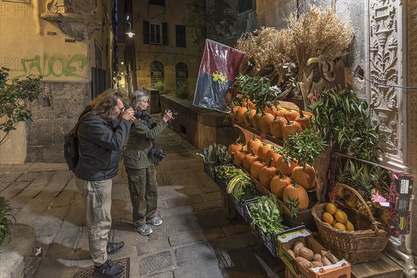 Tourists photographing a fruit shop in the evening in the historic centre, Genoa, Italy, Europe