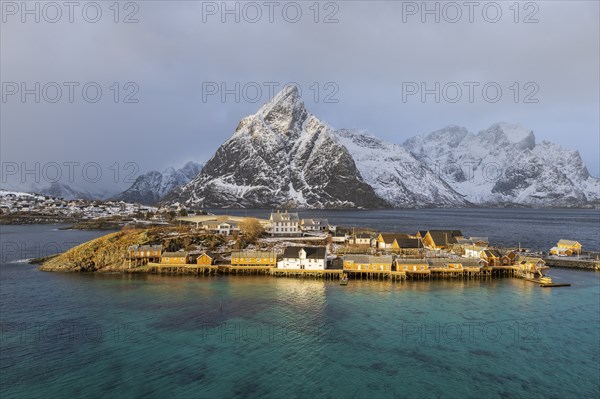 Traditional yellow rorbuer cabins on Sakrisoy Island, snow-capped rocky mountains in the back,