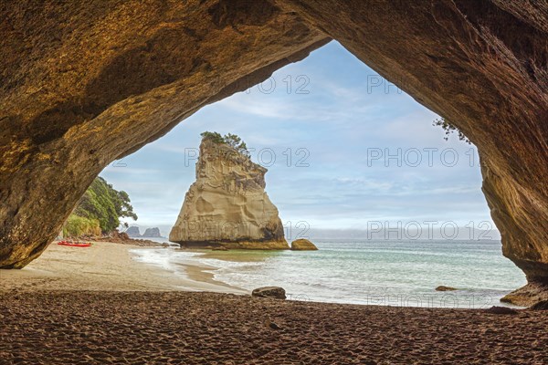 View through a rock arch onto a sandy beach and the sea with gentle waves, Cathedral Grove,