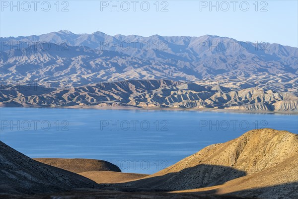 Blue Toktogul reservoir between dry mountain landscape, hilly mountains in the evening light,