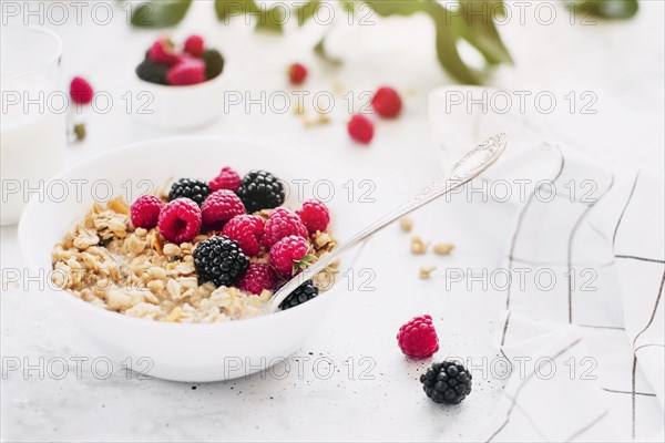 Morning healthy breakfast, white bowl full with granola, muesli, raspberry, blackberry on gray