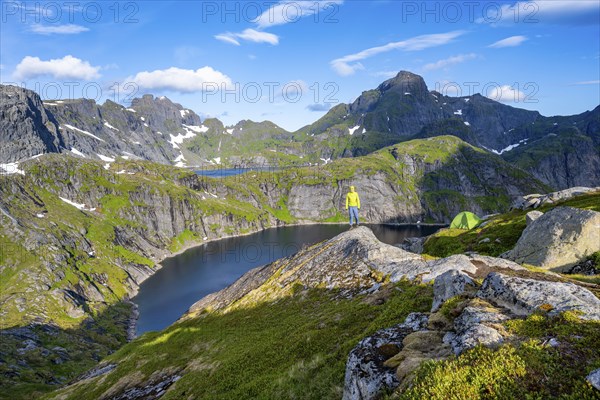 Mountaineer standing on a rock with green camping tent, mountain landscape with lake Tennesvatnet,