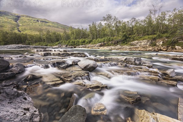 Abiskojakka, river in Abisko NP (northern Sweden) . Long exposure, rocks, birch, clouds, grey sky,