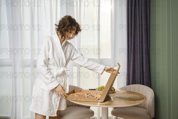 Cute woman in bathrobe opening pizza box