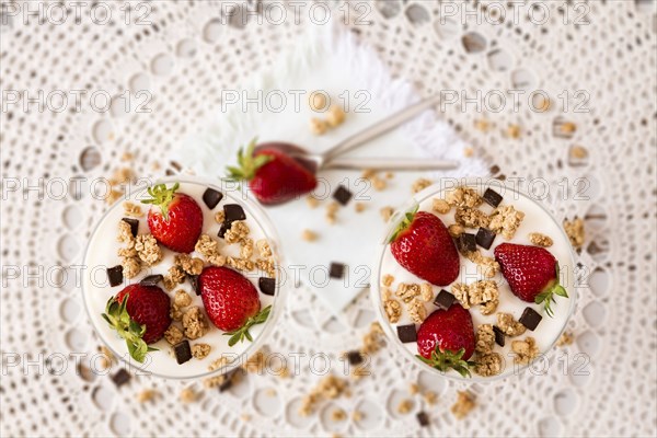 Strawberries cereals and chocolate flakes in two cups of plain yogurt seen from above