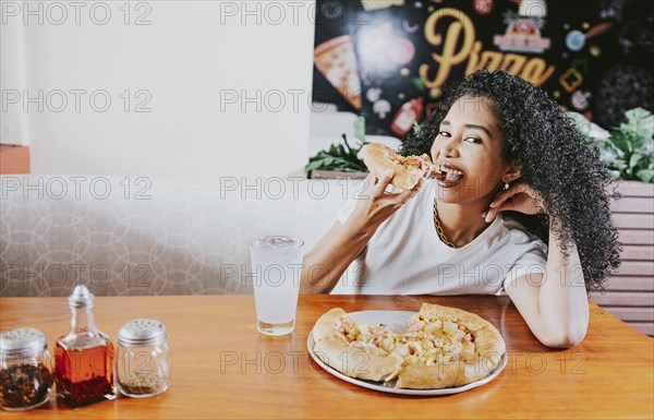 Smiling young woman enjoying a pizza in a restaurant. Happy afro hair girl eating pizza in a