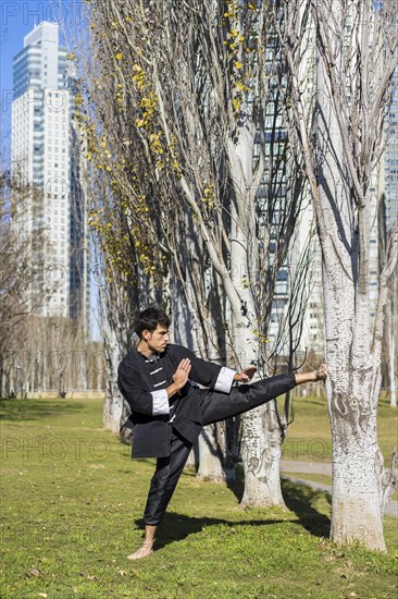 An athletic martial arts fighter practicing kicks in a public park.