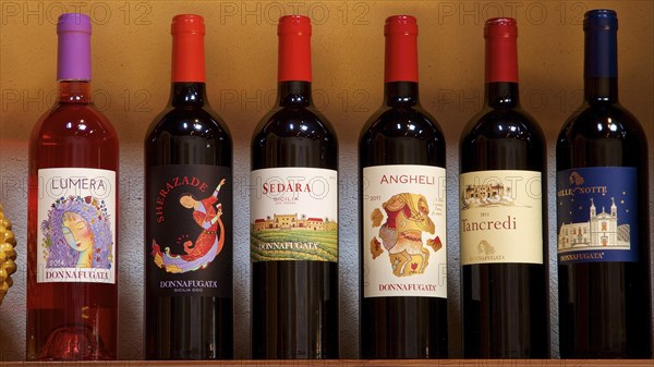 Various bottles of wine organised on a shelf, each with a unique label, Donna Fugata winery,