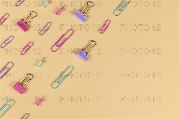 Stationery items like paper clips and drawing pins arranged on side of yellow background with empty
