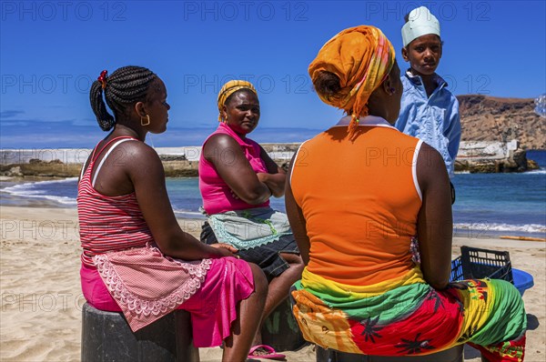 Dark skinned women, sitting at sandbeach and talking to each other. Tarrafal. Santiago. Cabo Verde.