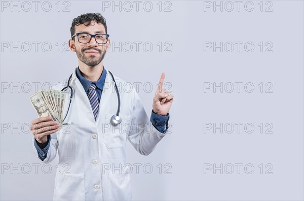 Handsome smiling doctor showing money and pointing side. Happy young doctor holding money and