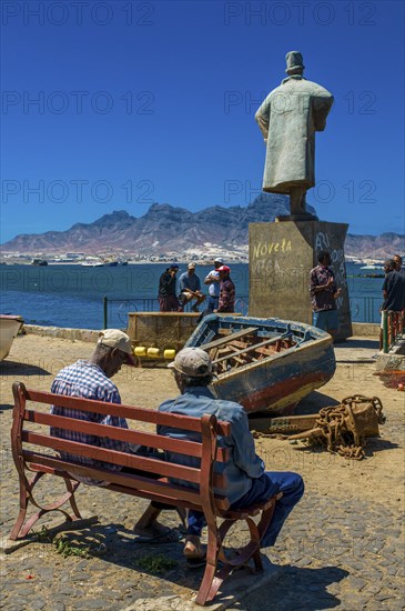 People sitting on bench in front of sculpture. San Vincente. Mindelo. Cabo Verde. Africa