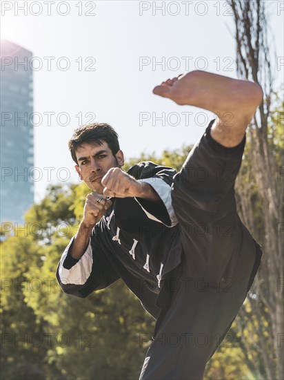 Handsome martial arts fighter practicing kicks outdoors while looking at camera