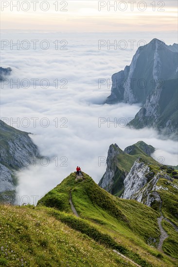 Two hikers enjoying the view over the Säntis mountains into the valley of Meglisalp at sunrise,