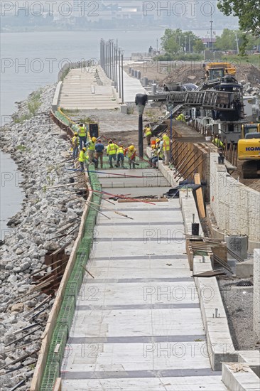 Workers pour cement to complete a section of the Detroit Riverwalk on the site of the former