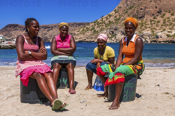 Dark skinned women, sitting at sandbeach and talking to each other. Tarrafal. Santiago. Cabo Verde.