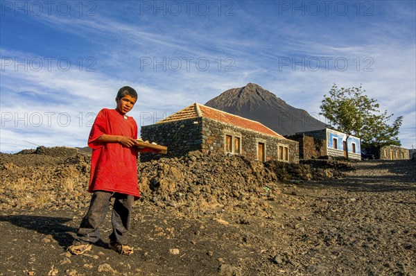Native boy selling something in front of his house, vulcano in background. Fogo. Cabo Verde. Africa