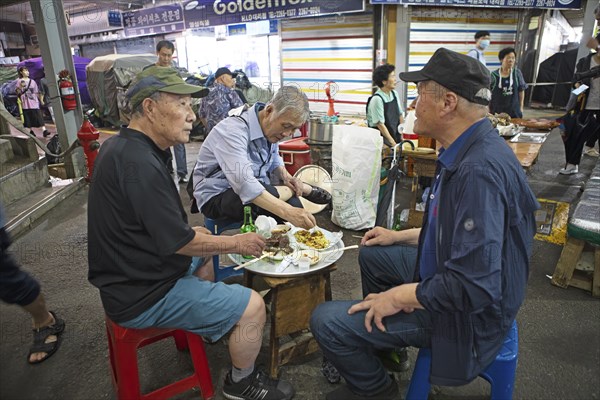 Old men sitting on plastic stools and eating at Gwangjang Market, traditional street market in