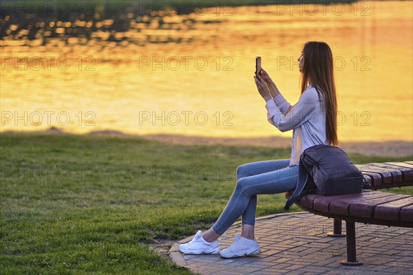 Blogger woman streaming online the beautiful sunset sitting on bench by river