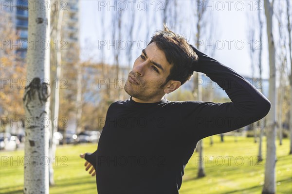 Sporty handsome man stretching neck and head after jogging in city public park