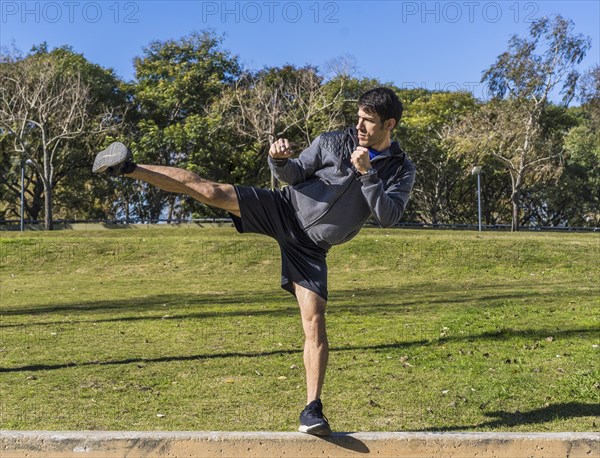 Young athletic martial arts fighter practicing kicks in a public park