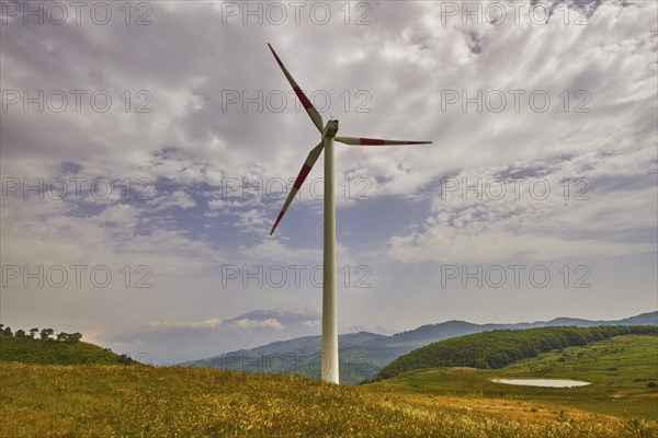 Single wind generator, meadow, green hills, cloudy blue sky, Nebrodi National Park, Sicily, Italy,