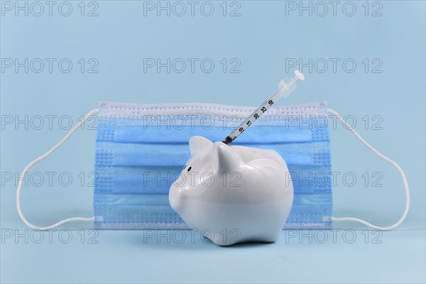 Corona virus vaccine expenses concept with white piggy bank, syringe and medical face mask on blue
