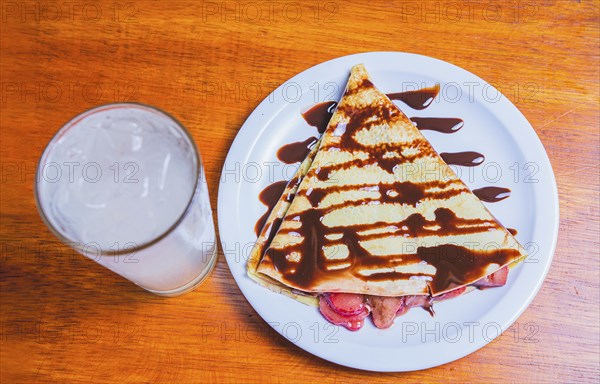 Crepe with chocolate cream and strawberry with drink on the table. Sweet strawberry crepe with