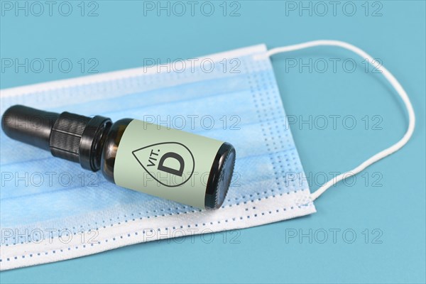 Medical face mask and bottle with vitamine drops on blue background