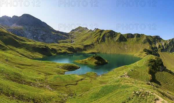 Schrecksee in the midst of green mountains under a clear sky, surrounded by lush vegetation and a