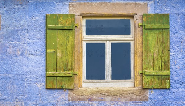 Aged wooden window and green shutters from an old german house with blueish painted wall stone