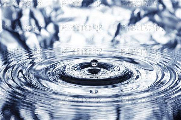 A drop of water falls onto the water surface and creates concentric circles, waves, rings