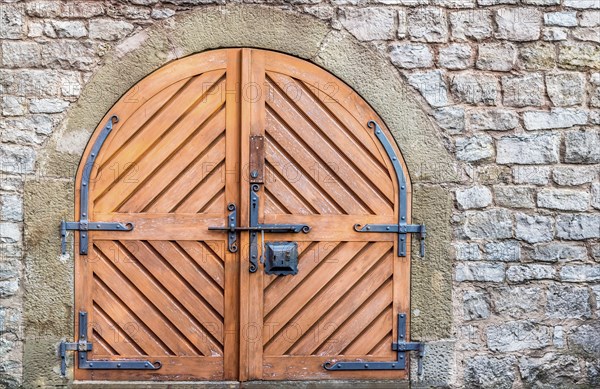 Ancient wooden door with metal hinged and latch, on a weathered stone wall