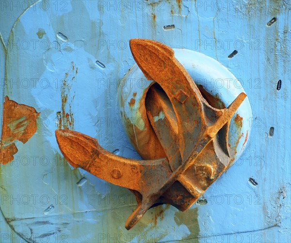 A massive anchor with rust is fastened on the side of a blue ship