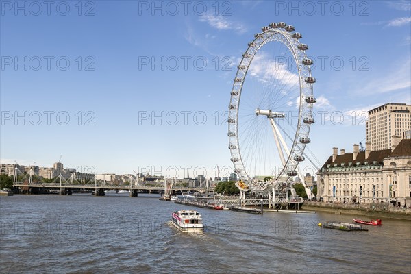 The Thames with boats and the London Eye Ferris wheel under a blue sky in London, United Kingdom,