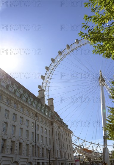 The London Eye Ferris wheel next to an old building under a blue sky with rays of sunshine, London,