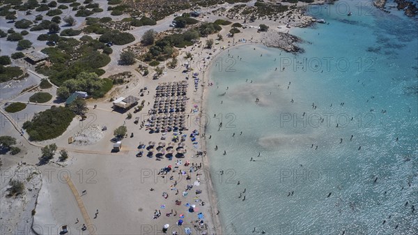 Overtourism, aerial view of a beach with people and umbrellas and a roof area next to the water,