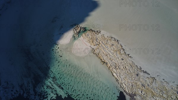 Drone image, aerial view of a narrow strip of sand in the turquoise sea next to a rock formation,