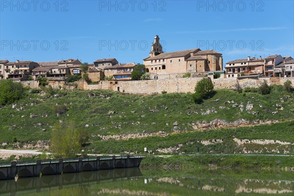 Historic town with church on a hill above a river with a stone bridge, the water reflects the