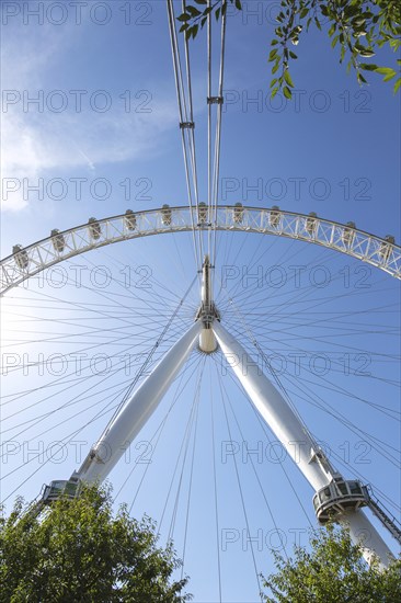 Close-up of the London Eye Ferris wheel and structure with trees and blue sky in the background,