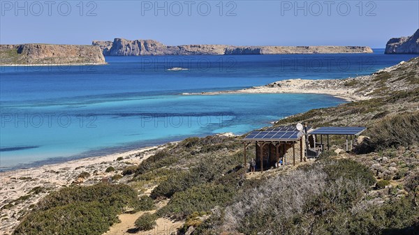 Caretaker building, coastal landscape with blue water, solar panels and green hills, quiet beach,