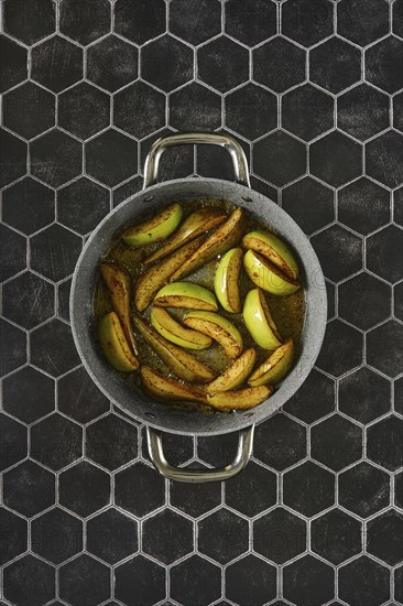 Sliced apples and pears caramelizing in a skillet with melted duck fat glaze on a hexagonal tile