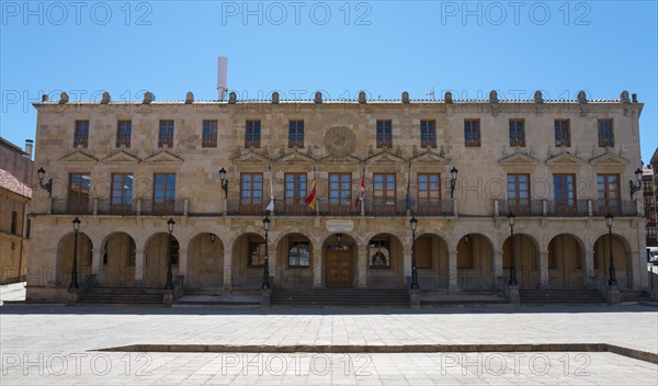 A large historic building with arcades and flags stretching across a spacious square under a blue