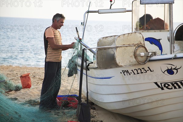 Fisherman in Armacao de Pera, Algarve, Portugal, fisherman preparing a net next to a boat on the
